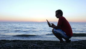 Силуэт человека на заходе солнца сидя на портовом районе с планшетом Оно проверяет сообщения от его видеоматериал Силуэт человека на заходе солнца сидя на портовом районе с планшетом Оно проверяет сообщения от его видеоматериал