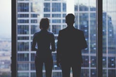 Силуэты вид сзади 2 деловых партнеров смотря заботливо из окна офиса в ситуации банкротства стоковая фотография Силуэты вид сзади 2 деловых партнеров смотря заботливо из окна офиса в ситуации банкротства стоковая фотография