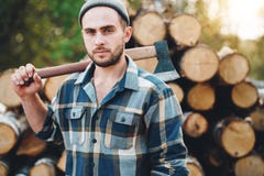 Сильный бородатый lumberman держит ось на его плече на складе журналов стоковая фотография rf Сильный бородатый lumberman держит ось на его плече на складе журналов стоковая фотография rf