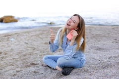 Симпатичная девушка тараторит на телефоне с улыбкой и сидит на пляже n стоковые изображения rf Симпатичная девушка тараторит на телефоне с улыбкой и сидит на пляже n стоковые изображения rf