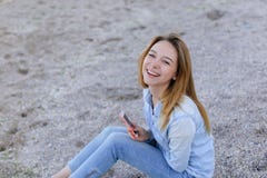 Симпатичная девушка тараторит на телефоне с улыбкой и сидит на пляже n стоковые изображения Симпатичная девушка тараторит на телефоне с улыбкой и сидит на пляже n стоковые изображения