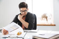 Сконцентрированный красивый человек в eyeglasses работая с документами стоковое фото Сконцентрированный красивый человек в eyeglasses работая с документами стоковое фото