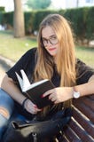 Сладкая белокурая девушка со стеклами смотря к вам и читая книгу в скамейке в парке стоковые изображения Сладкая белокурая девушка со стеклами смотря к вам и читая книгу в скамейке в парке стоковые изображения