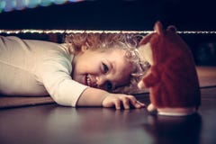 Смешной милый усмехаясь младенец играя прятк под кроватью с хомяком игрушки в винтажном стиле Стоковое фото RF Смешной милый усмехаясь младенец играя прятк под кроватью с хомяком игрушки в винтажном стиле Стоковое фото RF