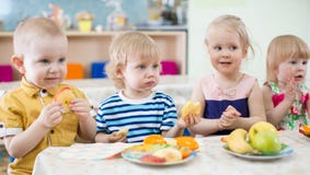 Смешные дети есть плодоовощи в комнате детского сада dinning стоковое изображение rf Смешные дети есть плодоовощи в комнате детского сада dinning стоковое изображение rf