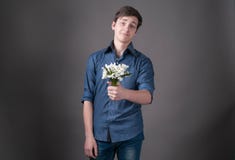 Смущенный молодой человек в голубой рубашке держа в букете с snowdrops, смотря камеру стоковое фото rf Смущенный молодой человек в голубой рубашке держа в букете с snowdrops, смотря камеру стоковое фото rf