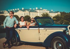 Состоятельные друзья приближают к классическому автомобилю с откидным верхом стоковое изображение Состоятельные друзья приближают к классическому автомобилю с откидным верхом стоковое изображение
