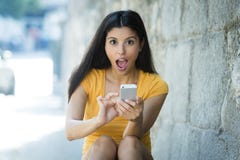 Сотрясенная и удивленная привлекательная молодая латинская женщина отправляя СМС и говоря на ее умном сотовом телефоне стоковое фото rf Сотрясенная и удивленная привлекательная молодая латинская женщина отправляя СМС и говоря на ее умном сотовом телефоне стоковое фото rf