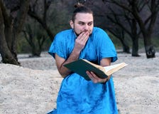 Сотрясенный красивый бородатый человек в голубой книге усаживания и чтения кимоно стоковые изображения rf Сотрясенный красивый бородатый человек в голубой книге усаживания и чтения кимоно стоковые изображения rf