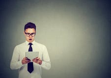 Сотрясенный молодой бизнесмен в стеклах используя планшет стоковая фотография Сотрясенный молодой бизнесмен в стеклах используя планшет стоковая фотография
