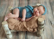 Спать newborn девушка, в деревянной кровати сделанной березы Усмехаться в сини связал костюм и шляпу стоковые изображения Спать newborn девушка, в деревянной кровати сделанной березы Усмехаться в сини связал костюм и шляпу стоковые изображения