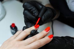 Специалист по маникюра в черных заботах перчаток о ногтях рук Manicurist красит ногти с красным маникюром стоковое фото Специалист по маникюра в черных заботах перчаток о ногтях рук Manicurist красит ногти с красным маникюром стоковое фото