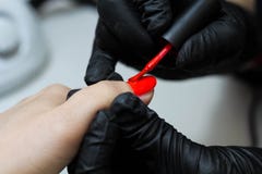Специалист по маникюра в черных заботах перчаток о ногтях рук Manicurist красит ногти с красным маникюром стоковая фотография rf Специалист по маникюра в черных заботах перчаток о ногтях рук Manicurist красит ногти с красным маникюром стоковая фотография rf