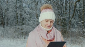 Средн-достигшая возраста женщина идет в парк зимы, наслаждается планшетом видеоматериал Средн-достигшая возраста женщина идет в парк зимы, наслаждается планшетом видеоматериал