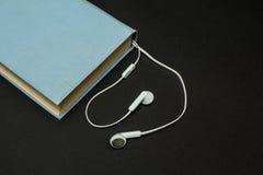 Старая голубая книга, и белые наушники на черной предпосылке стоковая фотография rf Старая голубая книга, и белые наушники на черной предпосылке стоковая фотография rf