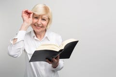 Старшая женщина стоит в комнате и читает книгу Она пробует выучить somethinf новое на выходе на пенсию потому что стоковая фотография Старшая женщина стоит в комнате и читает книгу Она пробует выучить somethinf новое на выходе на пенсию потому что стоковая фотография