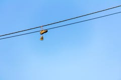 Старые тапки вися на электрическом проводе с голубым небом на заднем плане стоковые изображения Старые тапки вися на электрическом проводе с голубым небом на заднем плане стоковые изображения