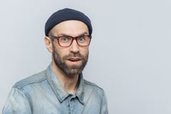 Стильная середина постарела мужчина с удивленный и любознательное выражение носит зрелища, куртку джинсовой ткани и шляпу, предст стоковое фото rf Стильная середина постарела мужчина с удивленный и любознательное выражение носит зрелища, куртку джинсовой ткани и шляпу, предст стоковое фото rf