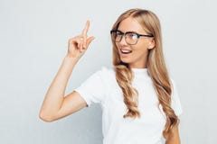 Студент девушки в стеклах, в белой футболке, сидящ на поле, имеющ идею и смотрящ камеру на серой предпосылке стены стоковые изображения Студент девушки в стеклах, в белой футболке, сидящ на поле, имеющ идею и смотрящ камеру на серой предпосылке стены стоковые изображения