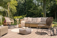 Стул Pouf и ротанга на деревянном патио с settee в саде во время лета Реальное фото стоковые фотографии rf Стул Pouf и ротанга на деревянном патио с settee в саде во время лета Реальное фото стоковые фотографии rf