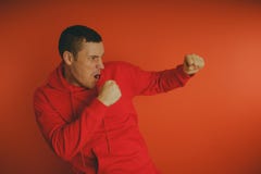 Сумасшедший и харизматический парень представляя на оранжевой предпосылке Человек в красном tracksuit стоковые изображения Сумасшедший и харизматический парень представляя на оранжевой предпосылке Человек в красном tracksuit стоковые изображения