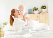 Счастливая мать семьи с играть младенца и объятие в кровати стоковое изображение rf Счастливая мать семьи с играть младенца и объятие в кровати стоковое изображение rf