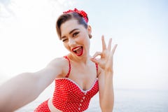 Счастливая милая девушка pinup в красном знаке о'кей показа купальника стоковая фотография Счастливая милая девушка pinup в красном знаке о'кей показа купальника стоковая фотография