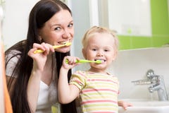 Счастливые мать и дочь ягнятся зубы девушки чистя щеткой Стоковые Фотографии RF Счастливые мать и дочь ягнятся зубы девушки чистя щеткой Стоковые Фотографии RF
