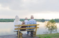 Счастливые родители и 2 малых дет сидя на стенде около озера стоковые фото Счастливые родители и 2 малых дет сидя на стенде около озера стоковые фото