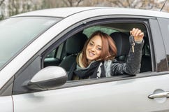 Счастливая молодая женщина сидя в автомобиле усмехаясь на камере показывая ключ стоковая фотография rf Счастливая молодая женщина сидя в автомобиле усмехаясь на камере показывая ключ стоковая фотография rf