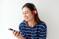 Счастливая молодая женщина смотря мобильный телефон и слушая к музыке с наушниками стоковая фотография rf Счастливая молодая женщина смотря мобильный телефон и слушая к музыке с наушниками стоковая фотография rf
