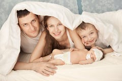 Счастливая семья на белой кровати в спальне Стоковые Фотографии RF Счастливая семья на белой кровати в спальне Стоковые Фотографии RF
