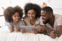 Счастливые африканские родители с дочерью используя планшет лежа на кровати стоковое фото rf Счастливые африканские родители с дочерью используя планшет лежа на кровати стоковое фото rf