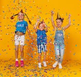 Счастливые дети на праздниках скача в пестротканый confetti на желтом цвете стоковые фото Счастливые дети на праздниках скача в пестротканый confetti на желтом цвете стоковые фото