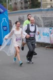 Счастливые заново пожененные пары бежать на улице города во время 5 км расстоянии марафона ATB Dnipro стоковое фото rf Счастливые заново пожененные пары бежать на улице города во время 5 км расстоянии марафона ATB Dnipro стоковое фото rf