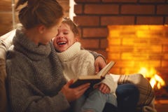 Счастливые мать семьи и дочь ребенка прочитали книгу на eveni зимы стоковое фото rf Счастливые мать семьи и дочь ребенка прочитали книгу на eveni зимы стоковое фото rf