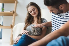 счастливые молодые пары petting кот дома пока сидящ стоковые фотографии rf счастливые молодые пары petting кот дома пока сидящ стоковые фотографии rf
