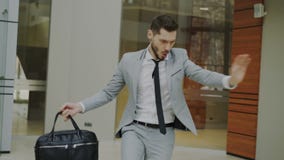 Счастливый и смешной бизнесмен с танцами портфеля в лобби офиса пока никто наблюдая его Счастливый и смешной бизнесмен с танцами портфеля в лобби офиса пока никто наблюдая его
