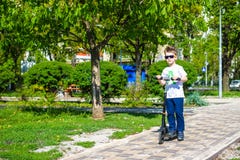 Счастливый мальчик едет скутер на дороге в парке стоковое изображение Счастливый мальчик едет скутер на дороге в парке стоковое изображение