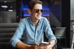 Счастливый молодой человек в стеклах, с телефоном в руке, сидя в кафе, соответствующем для рекламировать, ввод текста стоковое фото Счастливый молодой человек в стеклах, с телефоном в руке, сидя в кафе, соответствующем для рекламировать, ввод текста стоковое фото