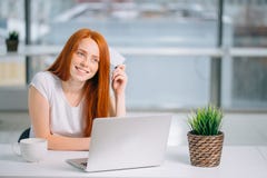 Счастливый покупатель redhead решая чего купить на линии держа усаживание кредитной карточки стоковая фотография Счастливый покупатель redhead решая чего купить на линии держа усаживание кредитной карточки стоковая фотография