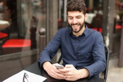 Счастливый человек сидя на таблице кафа и беседуя smartphone с стоковое изображение rf Счастливый человек сидя на таблице кафа и беседуя smartphone с стоковое изображение rf