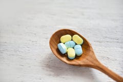 Таблетки медицины желтые и голубые в деревянной ложке на белой предпосылке деревянного стола в фармации стоковое фото rf Таблетки медицины желтые и голубые в деревянной ложке на белой предпосылке деревянного стола в фармации стоковое фото rf