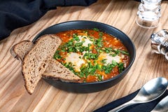 Традиционное израильское shakshuka блюда, томат взбитые яйца с овощами Закройте вверх на shakshuka в шаре с петрушкой и хлебом стоковые изображения Традиционное израильское shakshuka блюда, томат взбитые яйца с овощами Закройте вверх на shakshuka в шаре с петрушкой и хлебом стоковые изображения