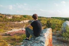 Турист молодого человека сидя на гигантском утесе, на верхней части горы стоковая фотография Турист молодого человека сидя на гигантском утесе, на верхней части горы стоковая фотография