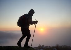 Туристский человек hiker с рюкзаком на скалистой горе на туманном голубом небе и поднимать предпосылку солнца стоковое фото Туристский человек hiker с рюкзаком на скалистой горе на туманном голубом небе и поднимать предпосылку солнца стоковое фото