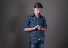 уверенный красивый молодой человек в голубой рубашке держа и используя смартфон на серой предпосылке стоковое изображение rf уверенный красивый молодой человек в голубой рубашке держа и используя смартфон на серой предпосылке стоковое изображение rf