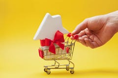 Укомплектуйте личным составом держать магазинную тележкау руки с лентой украшенной домом на желтой предпосылке Покупать новые дом стоковая фотография Укомплектуйте личным составом держать магазинную тележкау руки с лентой украшенной домом на желтой предпосылке Покупать новые дом стоковая фотография