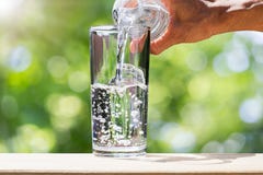 Укомплектуйте личным составом руку ` s держа воду бутылки питьевой воды и лить воду в стекло на деревянной столешнице на запачкан Стоковое Фото Укомплектуйте личным составом руку ` s держа воду бутылки питьевой воды и лить воду в стекло на деревянной столешнице на запачкан Стоковое Фото