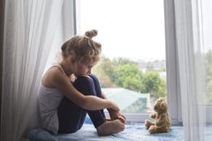 Унылая маленькая девочка сидит на силле окна и смотрит медведя стоковые изображения Унылая маленькая девочка сидит на силле окна и смотрит медведя стоковые изображения